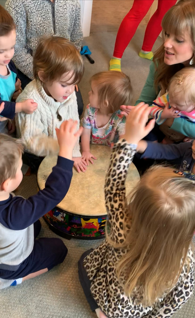 Teacher and young children making music together around a drum